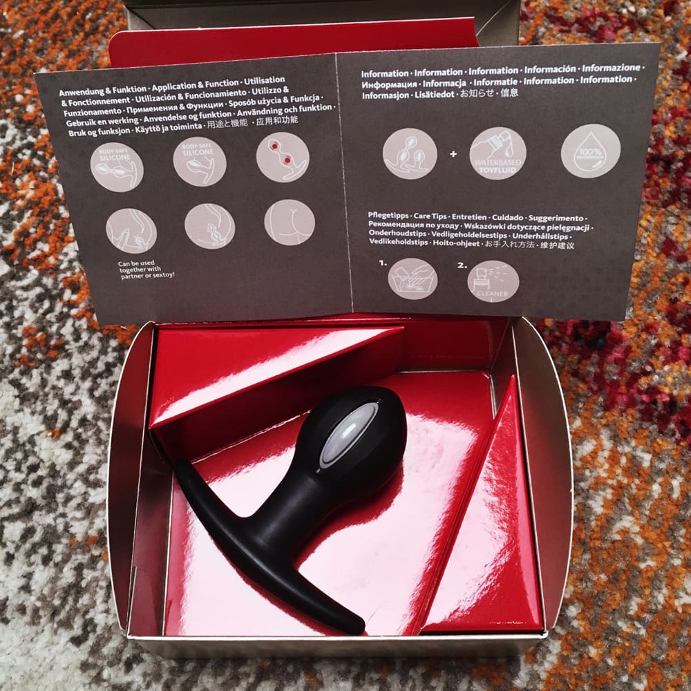 Photo of inside of the box showing inside of manual and black and grey butt plug