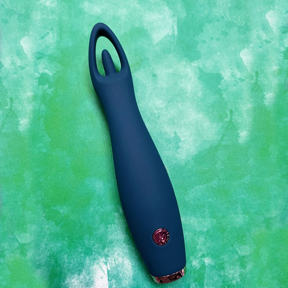 photograph of dark blue long thin vibrator on green background - oval shaped hoop around a small nub at the top, single silver button at the bottom